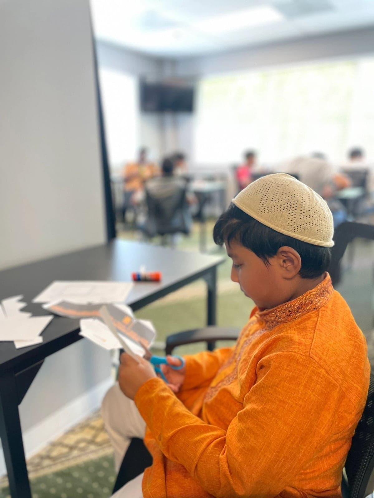 A young boy in a kufi and orange kurta working on a Kaaba craft