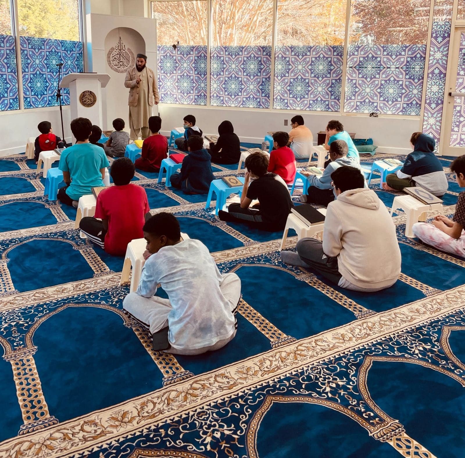 Children sitting in a halaqa on the prayer hall carpet listening to their teacher