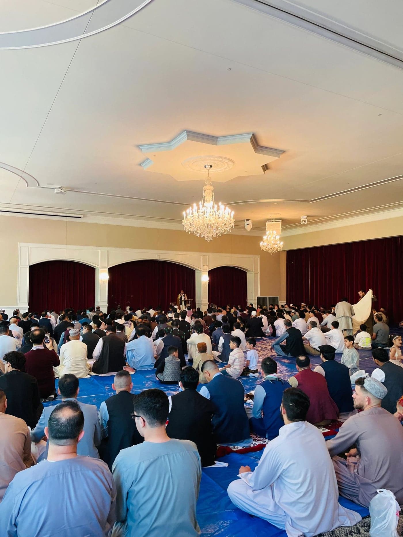 A large congregation of worshippers seated for prayer in a chandelier-lit hall