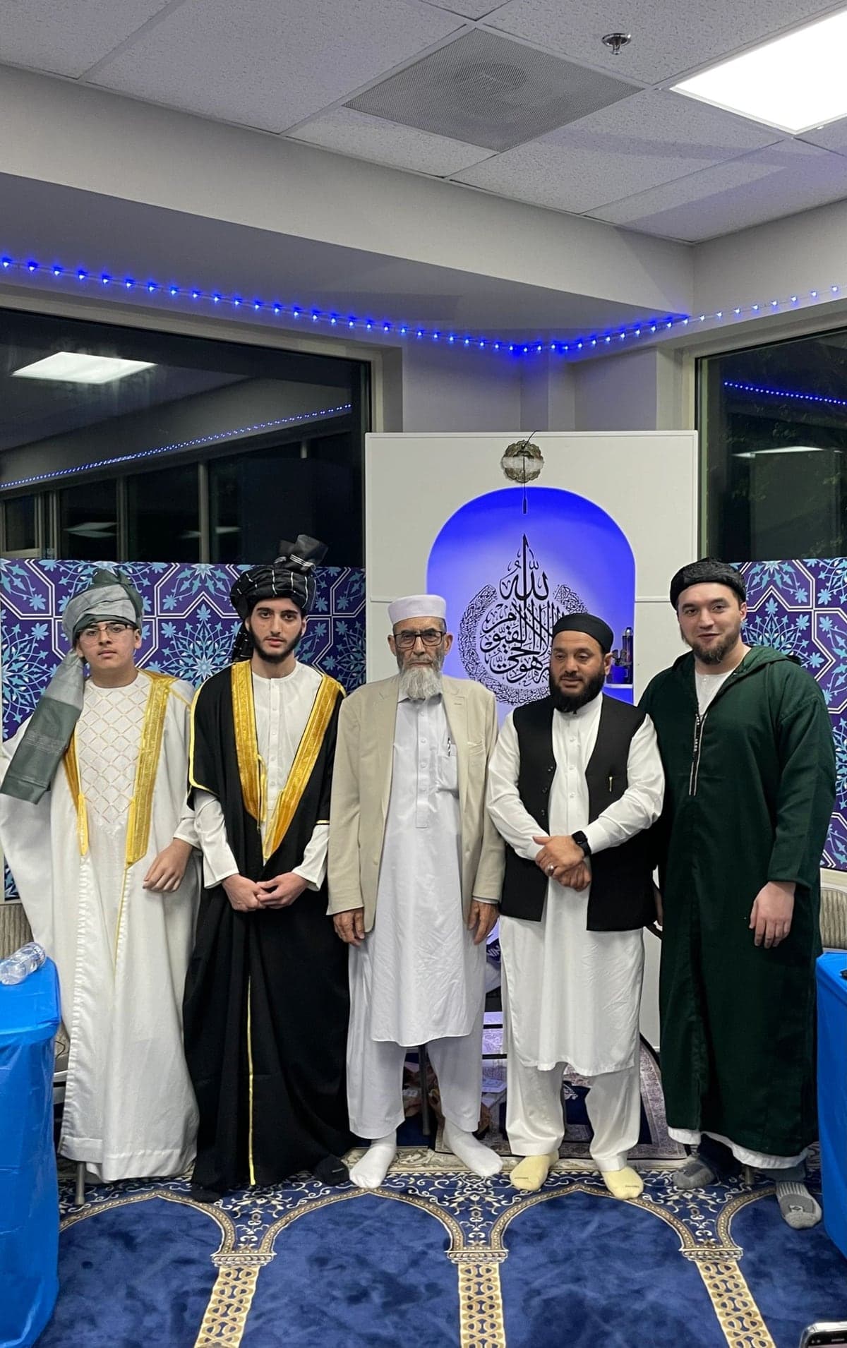 Qur'an graduates in ceremonial robes standing with scholars in front of the mihrab