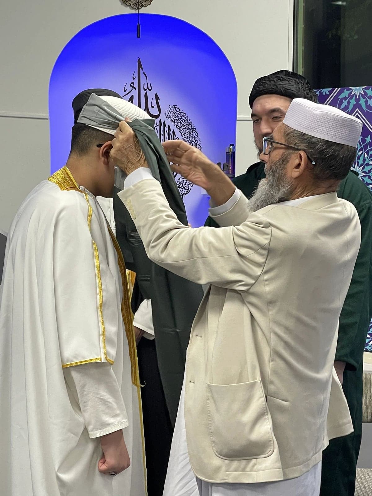 An elder places a turban on a young hafiz graduate during a ceremony