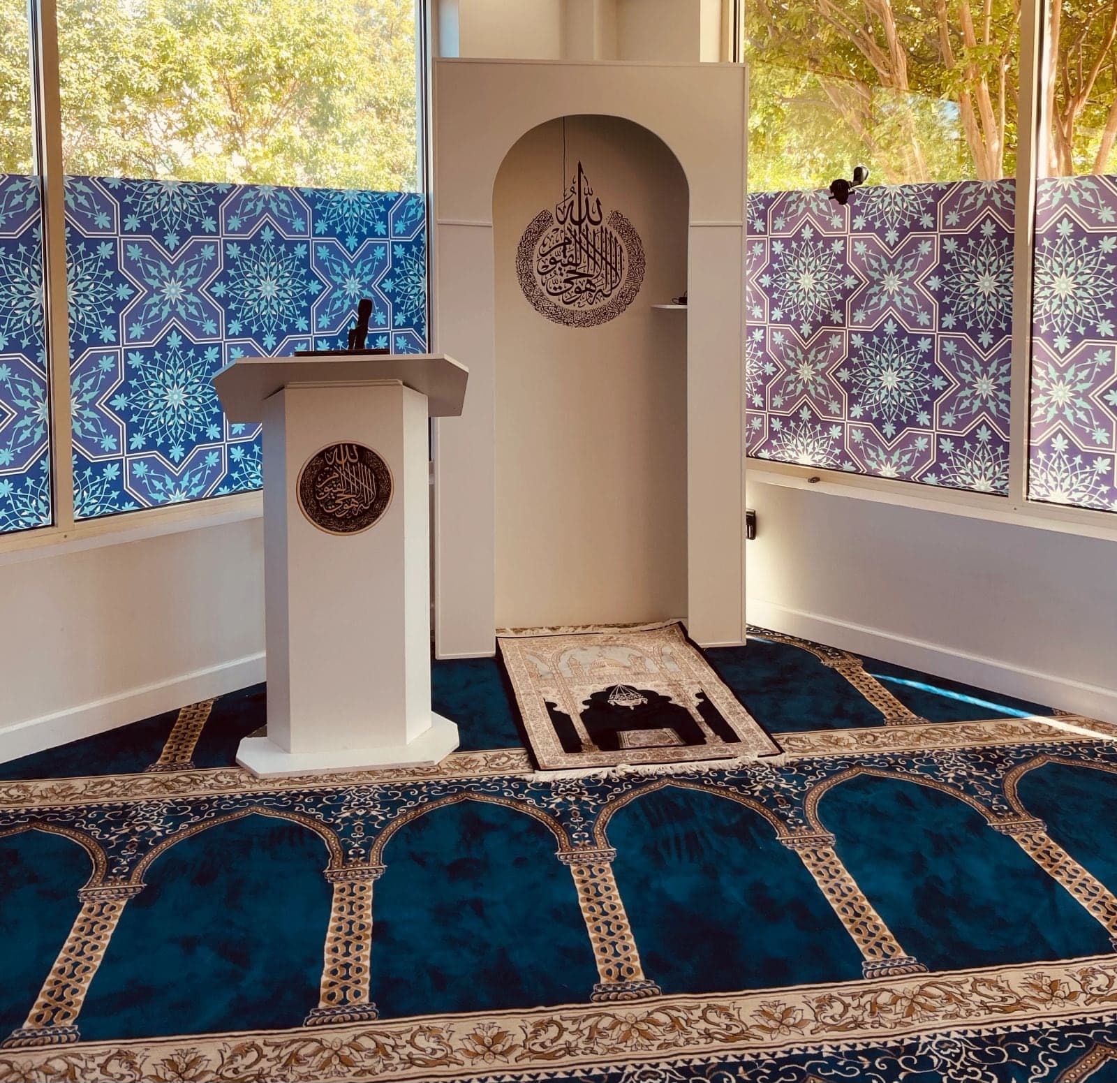 The AQSA Center prayer hall in daylight, with its white mihrab, minbar and blue patterned windows