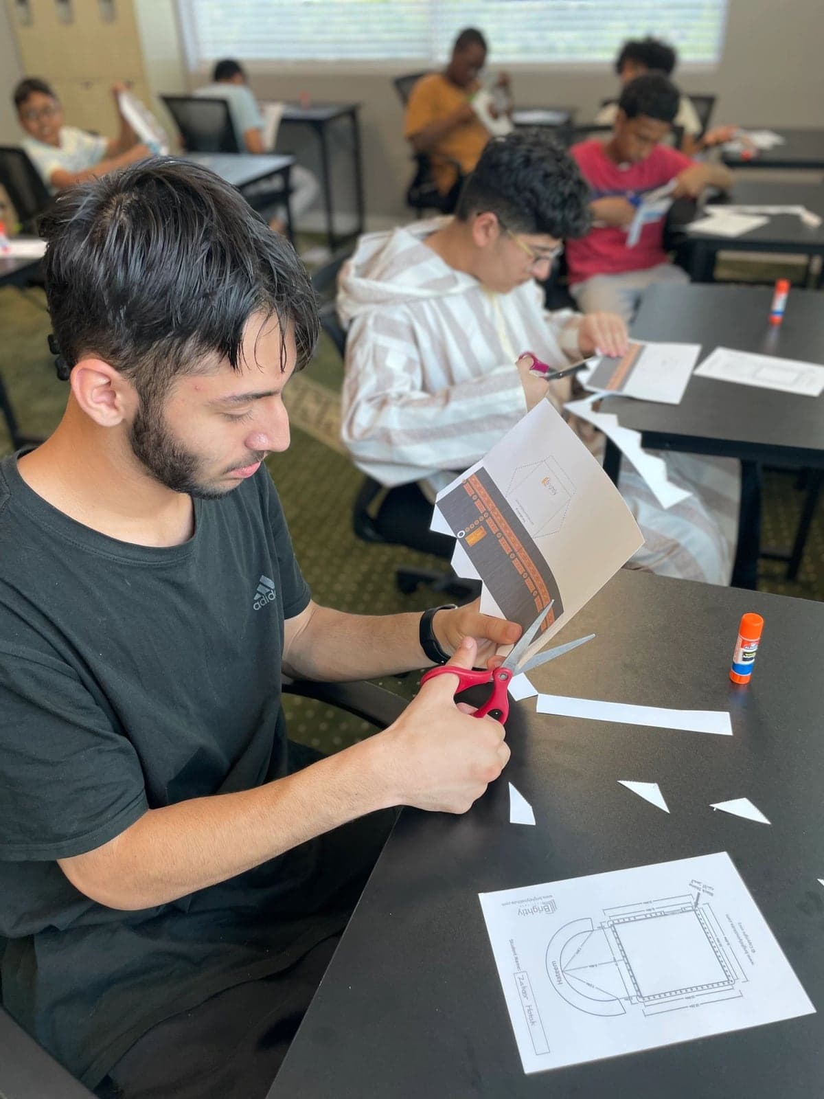 Young adults cutting and folding Kaaba models at the center