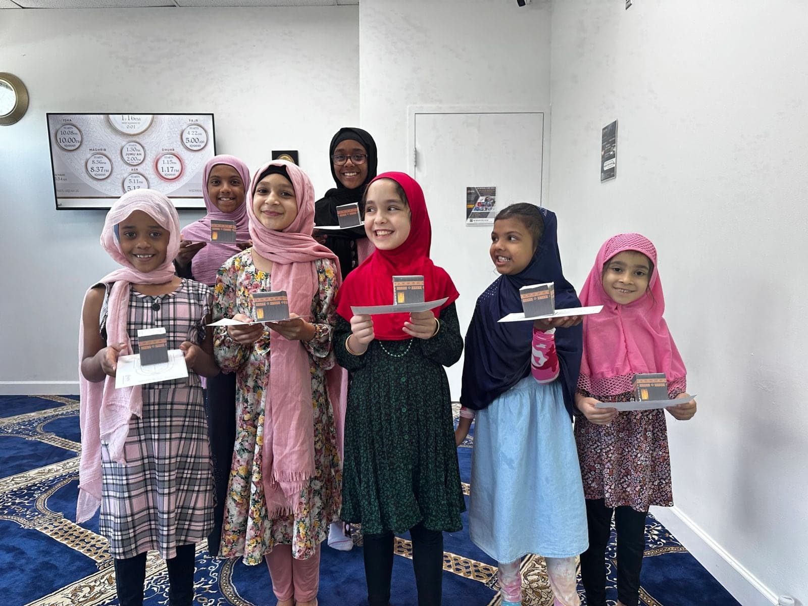 Young girls in hijabs smiling as they hold their Qur'an program certificates
